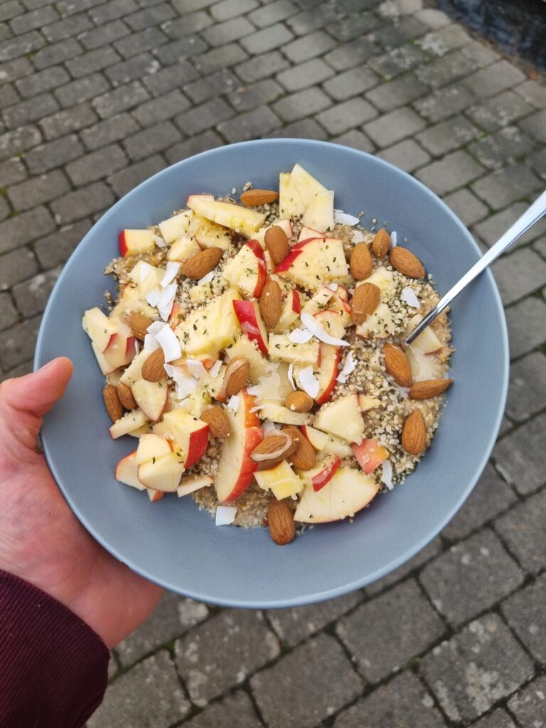 Skål med gröt som är toppad med skivade äpplen, mandlar, kokosflakes, och honung.