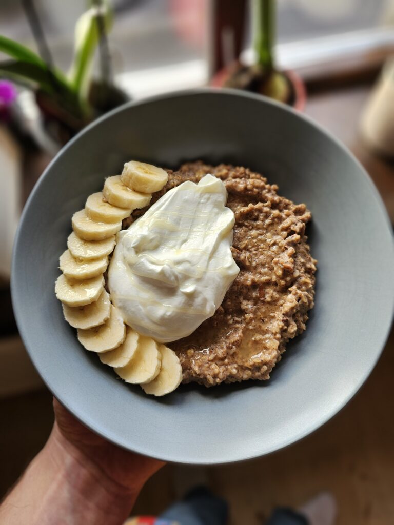 Tallrik med krämig gröt toppad med banan, kvarg, hackade nötter, och honung