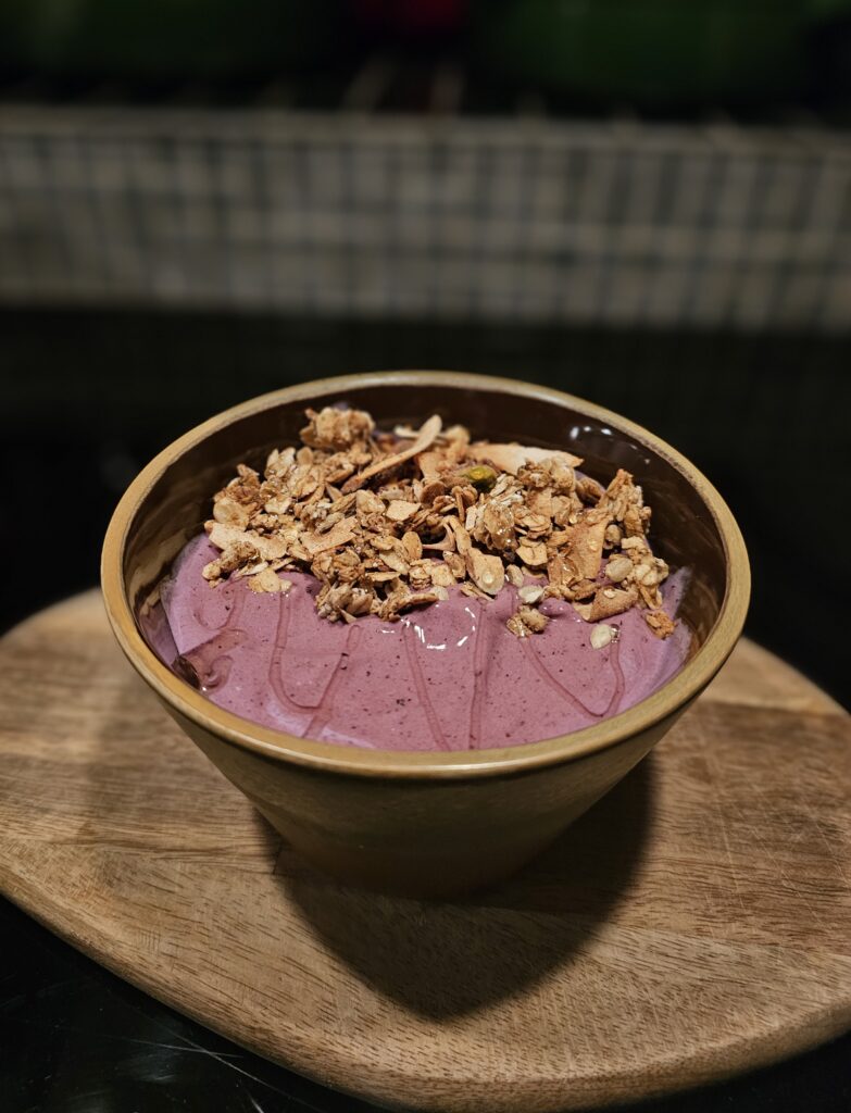 Skål med lila smoothie, toppad med kokos, granola, och honung.