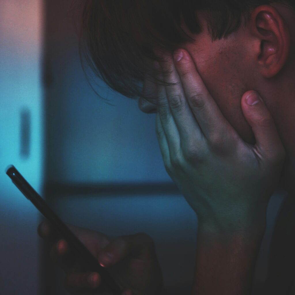 Trött person som sitter och tittar på sin smartphone samtidigt som han håller för huvudet.